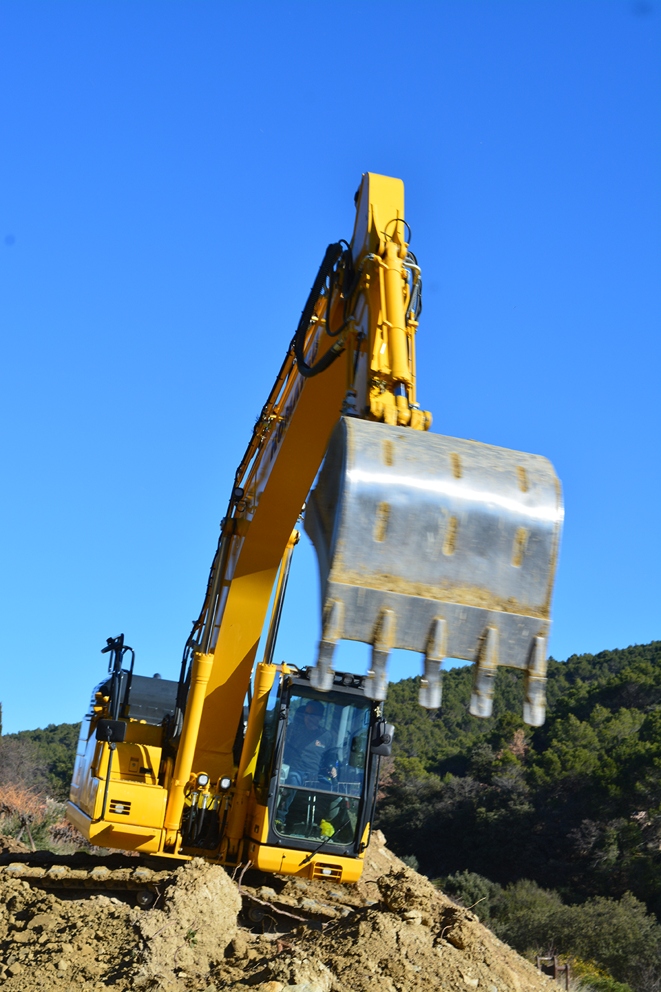 Pelle 23 Tonnes, gros plan sur le godet et machine en arrière plan lors d'un terrassement pour création de restanque. Terrassement, VRD, assainissement et enrochement